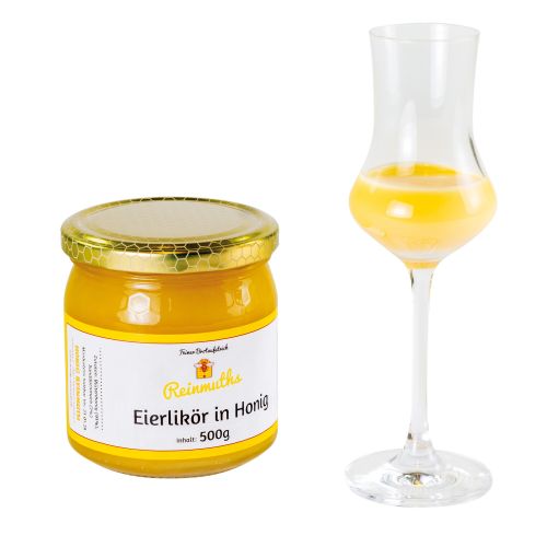 Glas mit goldenem Deckel mit Wabenmuster mit Etikett Eierlikör in Honig davor ein Schnapsglas mit langem Stil gefüllt mit Eierlikör