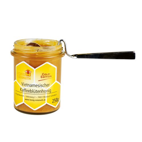 offenes Glas mit Honig ein Edelstahlhoniglöffel eingehängt.