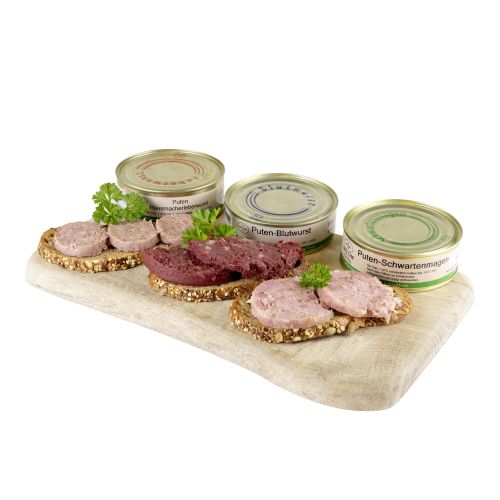 Holzbrettchen darauf 3 Wurstdosen nebeneinander, davor je eine Scheibe Brot belegt mit Wurst dekoriert mit Petersilie